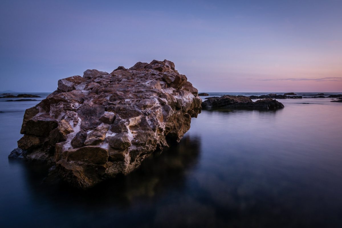 Large coastal rock formation in calm water at sunset